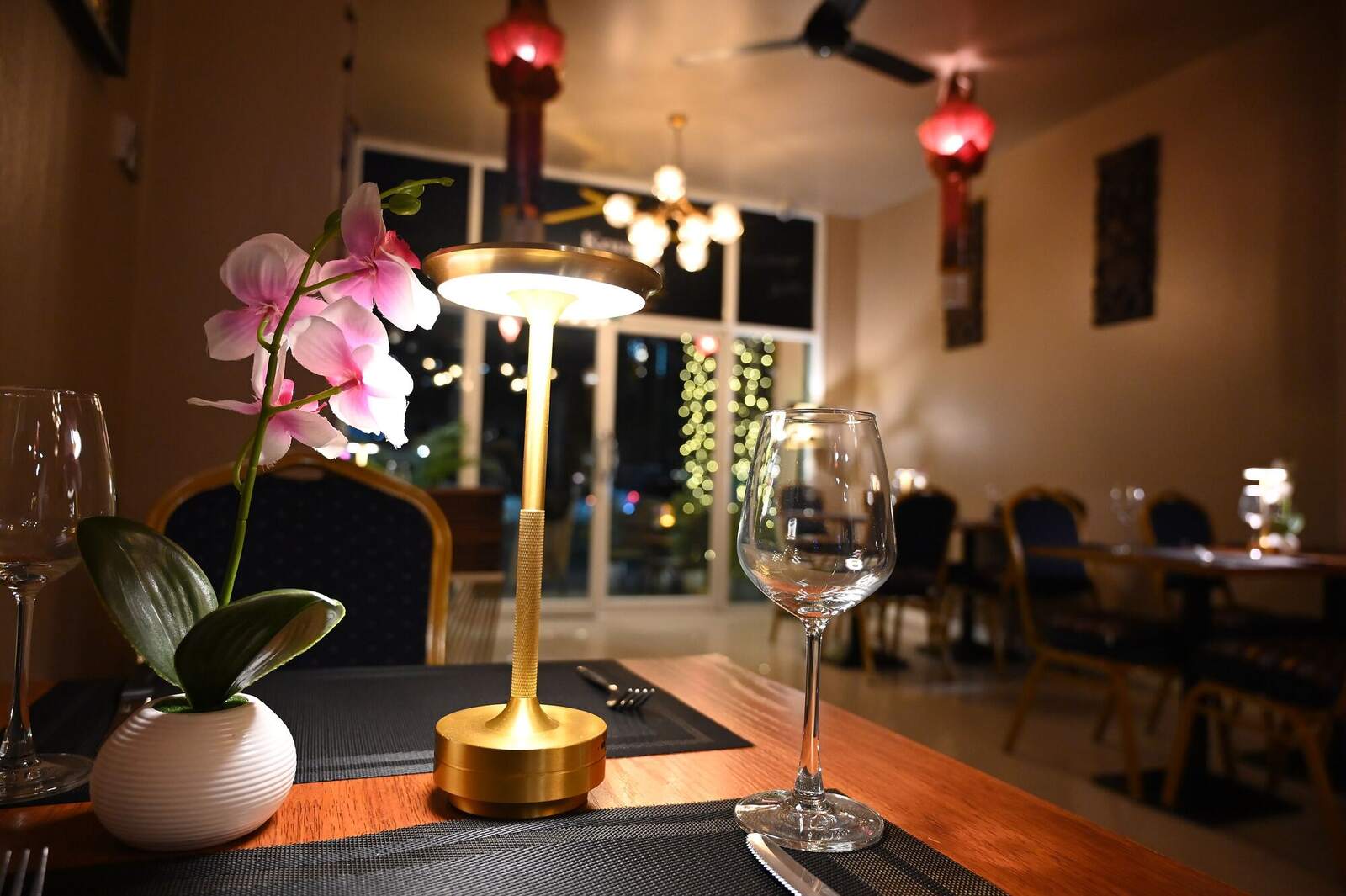 A lamp-lit dining table with wine glasses in a warm, softly lit room