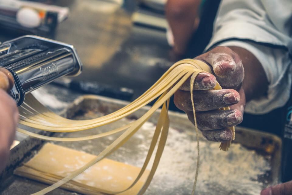 A chef's floury hands lifting freshly cut ribbons of pasta