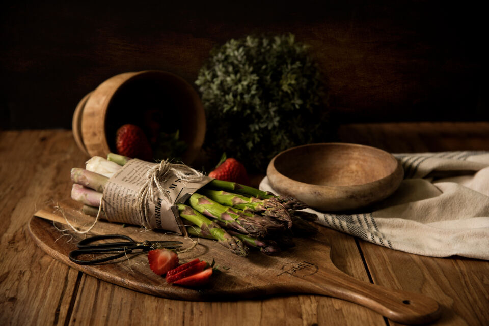 Rustic still life of asparagus, herbs and wooden bowls on a dark table
