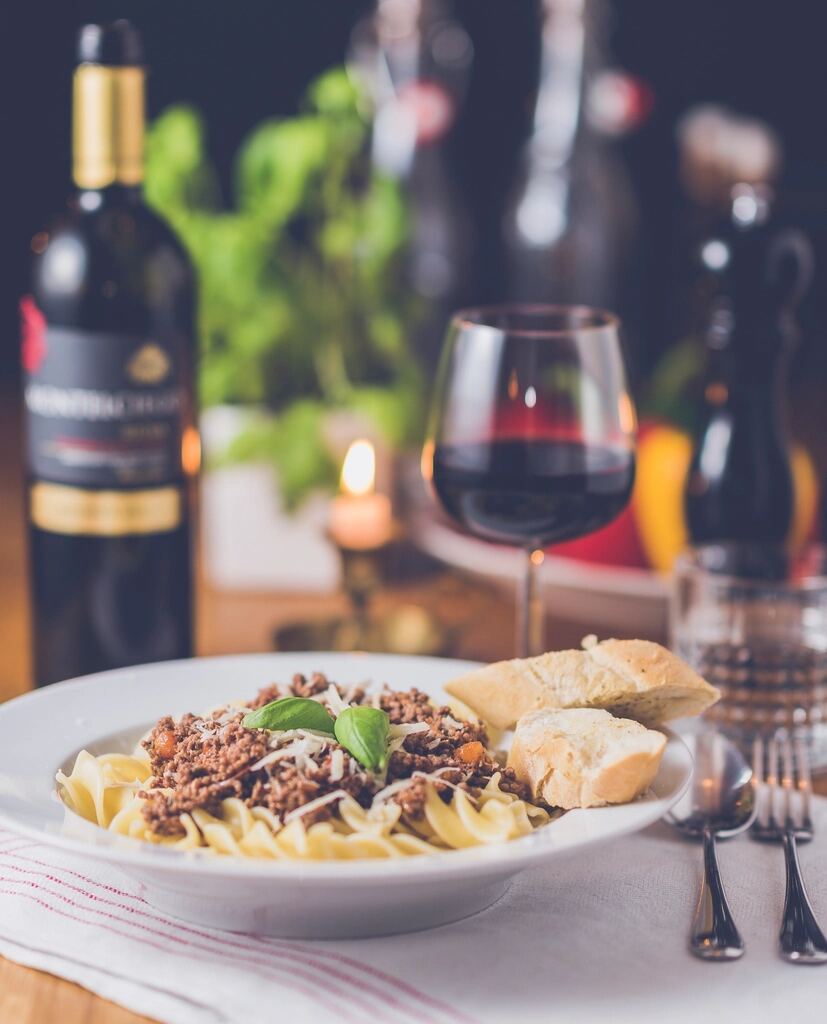 A plate of pasta beside a glass of red wine and a candle